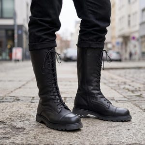 Puede incluir: Un par de botas negras de media caña con cierre frontal de cordones finos negros, puntera redondeada y suela de goma gruesa con tacos. Las botas llegan hasta la mitad de la pantorrilla y están confeccionadas en un material negro mate liso.