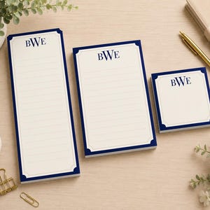 May include: Three cream-colored paper notepads of varying sizes, each featuring a dark blue border and the monogram BWE printed in dark blue at the top. The two larger pads are rectangular with horizontal lines, while the smallest is square.
