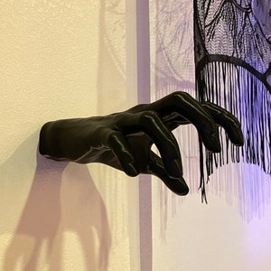 May include: A black, 3D printed hand sculpture mounted on a white wall. The hand is reaching out with fingers extended, as if grabbing something.
