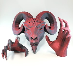 May include: A red, black, and gray 3D printed sculpture of a goat head with horns and a hand. The goat head has a pentagram on its forehead. The hand is in a grasping position.