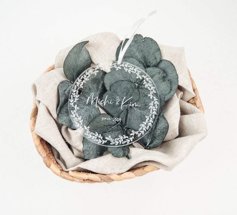 May include: A clear round ornament with a white wreath design and the text "Michi & Kim since 2009" on a white background.