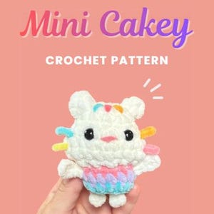 Op de afbeelding: Een wit gehaakt knuffeltje met zwarte ogen, een roze neus en kleurrijke accenten op het hoofd en de zijkanten. Het speelgoed draagt een rokje in pasteltinten. De tekst erboven luidt Mini Cakey CROCHET PATTERN in wit en paars op een perzikkleurige achtergrond.