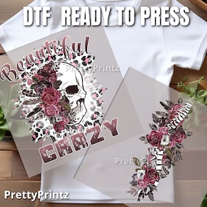 May include: A white t-shirt with a pink and black leopard print design featuring a skull with flowers and the text "Beautiful Crazy".