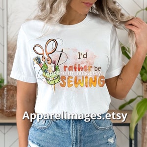 May include: White t-shirt with a watercolor design of sewing tools and the text "I'd rather be sewing".