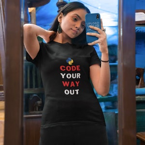 May include: A woman wearing a black t-shirt with the text "CODE YOUR WAY OUT" and a python logo in red, yellow, and blue. The woman is taking a selfie in a mirror.
