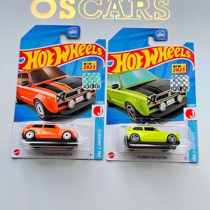 Puede incluir: Dos coches de juguete Hot Wheels en embalaje azul. Uno es naranja con capó negro, el otro verde con capó negro. Ambos están etiquetados como '73 Honda Civic Custom' y 'HW J-Imports'. El embalaje dice 'Nuevo para 2023'.