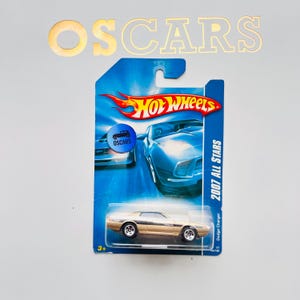 May include: A gold-colored 2007 Dodge Charger Hot Wheels die-cast car on a blue and white card. The card features the Hot Wheels logo and the text "2007 All Stars". The word "OSCARS" is visible in gold letters above the card.
