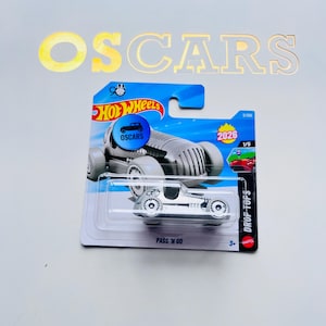 以下が含まれることがあります： オリジナルのパッケージに入ったシルバーのホットウィールのおもちゃの車。この車は、大きなホイールと「PASS 'N GO」の文字が入ったヴィンテージスタイルのレーサーです。パッケージには、ホットウィールのロゴ、「OSCARS」の文字、数字「2026」が含まれています。
