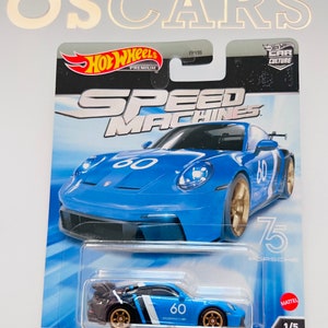 May include: A blue and black Hot Wheels Speed Machines die-cast toy car, a Porsche 911 GT3, with a white number 60 on the side. The car is on a blue and white background with the words "Speed Machines" and "Porsche 911 GT3".