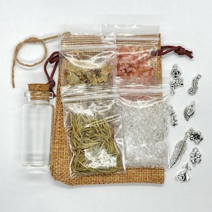 May include: A burlap bag with a clear glass bottle, cork stopper, and various small plastic bags filled with herbs, crystals, and pink salt. Silver charms in floral and feather designs are scattered around the bag. The bag is tied with a brown cord.
