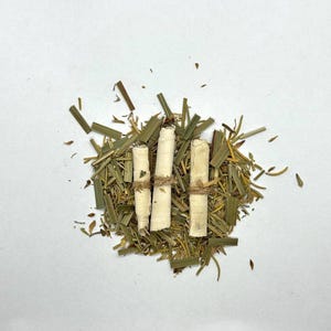 May include: Three rolled white items tied with twine, surrounded by dried green and yellow herbs. The items appear to be tightly rolled, possibly for a specific purpose. The herbs are scattered around the items, creating a natural, earthy aesthetic.