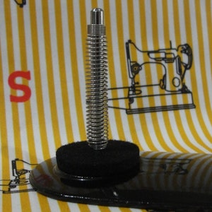 May include: A black sewing machine foot with a spring-loaded metal rod. The foot is designed to be used with a sewing machine.