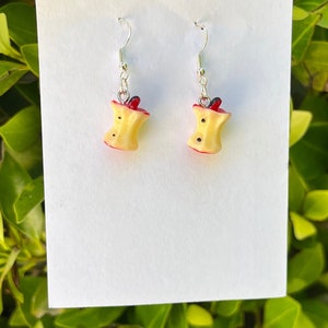 May include: A pair of silver dangle earrings featuring a red and yellow bitten apple design.