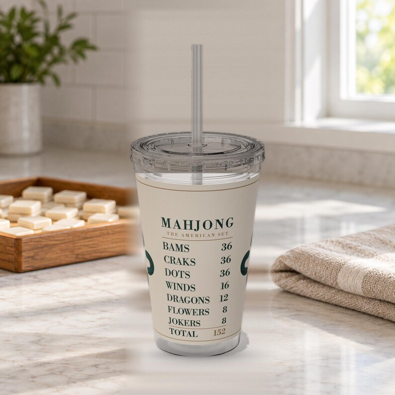 Puede incluir: Un vaso de pl&aacute;stico transparente con tapa y pajita, que presenta una banda de color crema impresa con texto verde oscuro que dice Mahjong The American Set, seguido de una lista de categor&iacute;as de juego y valores num&eacute;ricos que suman 152.
