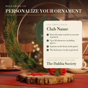 May include: A circular ornament display featuring a green pine branch on a wood slice base. An overlay provides instructions for personalizing a club name, with a 18-character limit, and displays the example text The Dahlia Society.