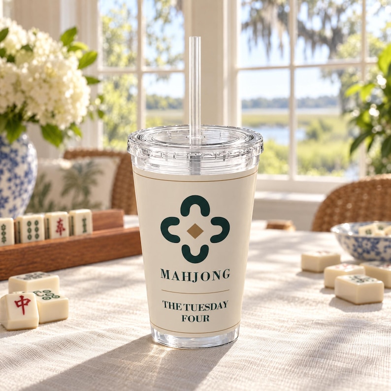 May include: A clear plastic tumbler with a lid and straw, featuring a cream-colored wrap with a dark green four-leaf clover-like icon, the word MAHJONG, and the text THE TUESDAY FOUR printed in dark green lettering on the front surface.