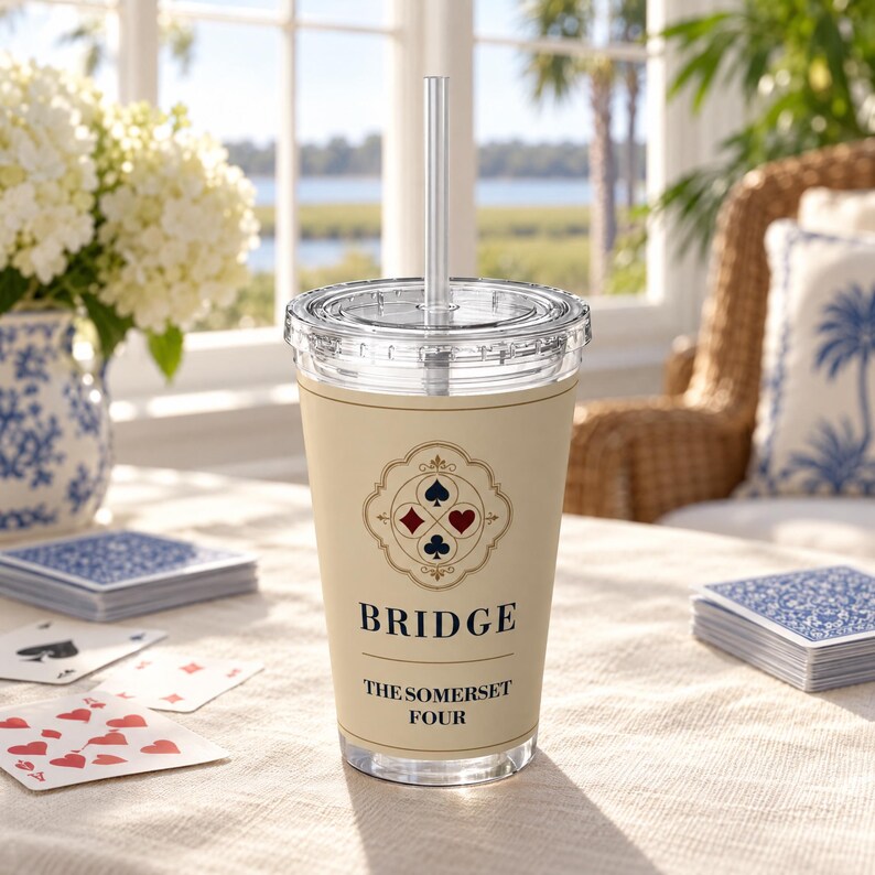 May include: A clear plastic tumbler with a lid and straw, featuring a beige wrap printed with a decorative emblem of four card suits, the word BRIDGE, and the text THE SOMERSET FOUR. The design includes a black spade, red diamond, red heart, and black club.