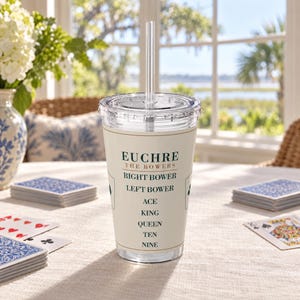 May include: A clear plastic tumbler with a lid and straw, featuring a cream-coloured label printed with the text EUCHRE THE BOWERS, RIGHT BOWER, LEFT BOWER, ACE, KING, QUEEN, TEN, NINE in dark green lettering, surrounded by playing card suit icons.