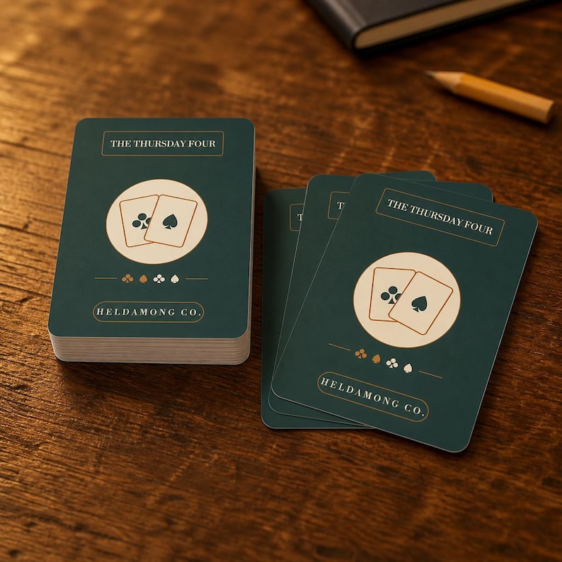 Puede incluir: Una baraja de cartas con fondo verde oscuro y un c&iacute;rculo central de color crema. Las cartas presentan el texto THE THURSDAY FOUR y HELDAMONG CO. junto con un gr&aacute;fico de dos cartas que muestran un s&iacute;mbolo de tr&eacute;bol y una pica.
