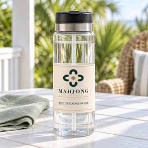Peut inclure: Une bouteille d'eau en plastique transparent avec un couvercle noir et une bande m&eacute;tallique argent&eacute;e. La bouteille pr&eacute;sente une &eacute;tiquette cr&egrave;me avec une ic&ocirc;ne de tr&egrave;fle vert fonc&eacute;, un petit losange dor&eacute; et le texte MAHJONG et THE TUESDAY FOUR.