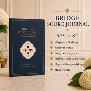 May include: A dark blue softcover Bridge Score Journal measuring 14.6 cm by 20.3 cm. The cover features gold text, a central emblem with four card suit symbols, and the brand name HELDAMONG CO. The journal contains 100 pages for notation and scores.