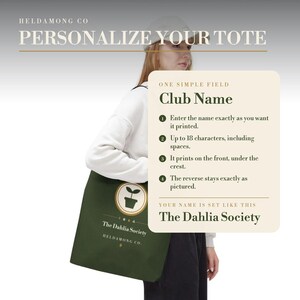 Op de afbeelding: Een donkergroene tote bag met een rond logo met een icoon van een plant in een pot en de tekst The Dahlia Society en HELDAMONG CO. Een overlay-venster geeft instructies voor het personaliseren van een clubnaam, met een limiet van 18 tekens.