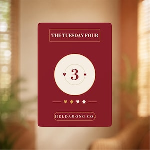 May include: A rectangular card with a deep red background featuring the text THE TUESDAY FOUR at the top. A central cream circle displays the number 3 flanked by small heart and diamond symbols. Below, a row of suit icons and HELDAMONG CO. text.