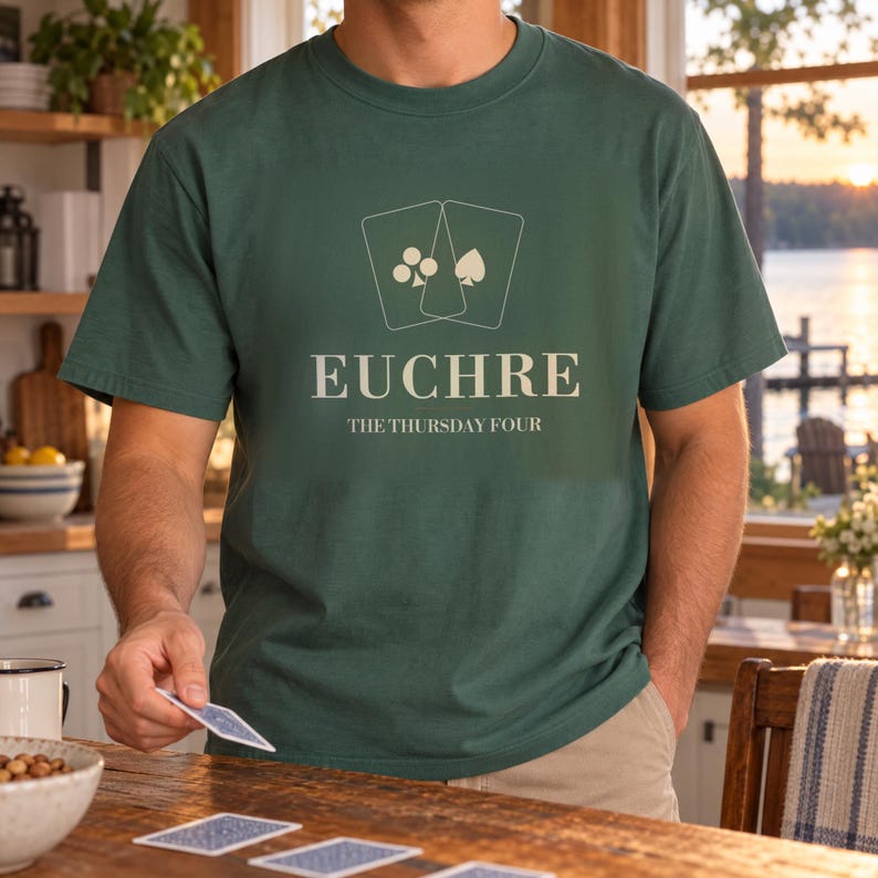 May include: A dark green short-sleeve t-shirt featuring a white graphic of two playing cards with club and spade symbols. Below the cards, the text reads EUCHRE and THE THURSDAY FOUR in a clean, sans-serif font centered on the chest area.