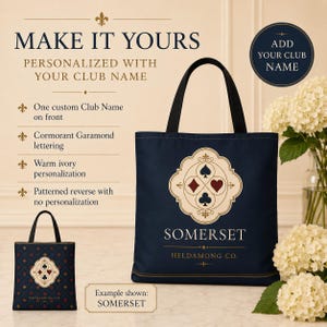 May include: A navy blue tote bag featuring a central cream-coloured emblem with four playing card suit symbols in red and black. The text SOMERSET and HELDAMONG CO. is printed in warm ivory. The reverse side displays a repeating pattern of suits.