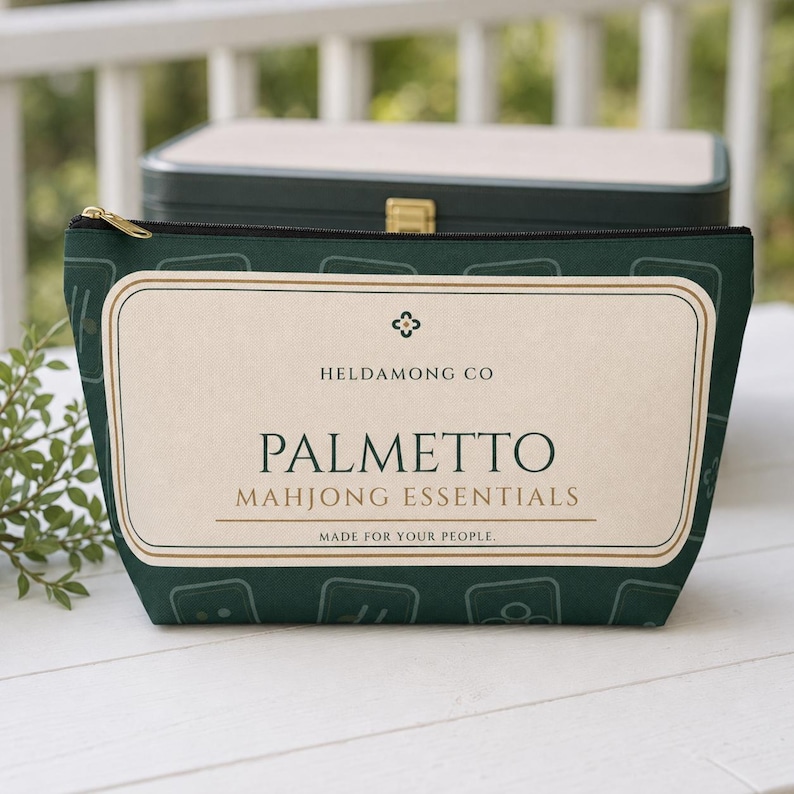 以下が含まれることがあります： HELDAMONG CO、PALMETTO MAHJONG ESSENTIALS、MADE FOR YOUR PEOPLEという文字が記されたクリーム色の長方形ラベルが付いたダークグリーンのファスナー付きポーチ。ポーチには、明るい緑色の麻雀牌の輪郭が繰り返されるパターンが施されています。
