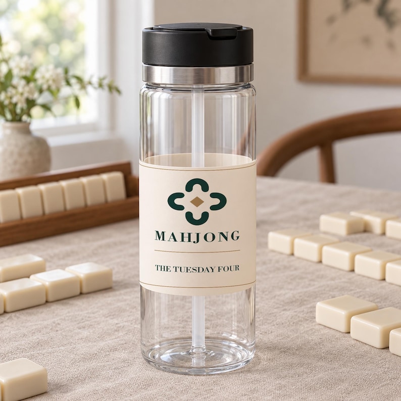 Peut inclure: Une bouteille d'eau en plastique transparent avec un couvercle noir et un anneau en m&eacute;tal argent&eacute;. La bouteille pr&eacute;sente une &eacute;tiquette cr&egrave;me avec une ic&ocirc;ne de tr&egrave;fle vert fonc&eacute;, le mot MAHJONG et le texte THE TUESDAY FOUR en vert fonc&eacute;.