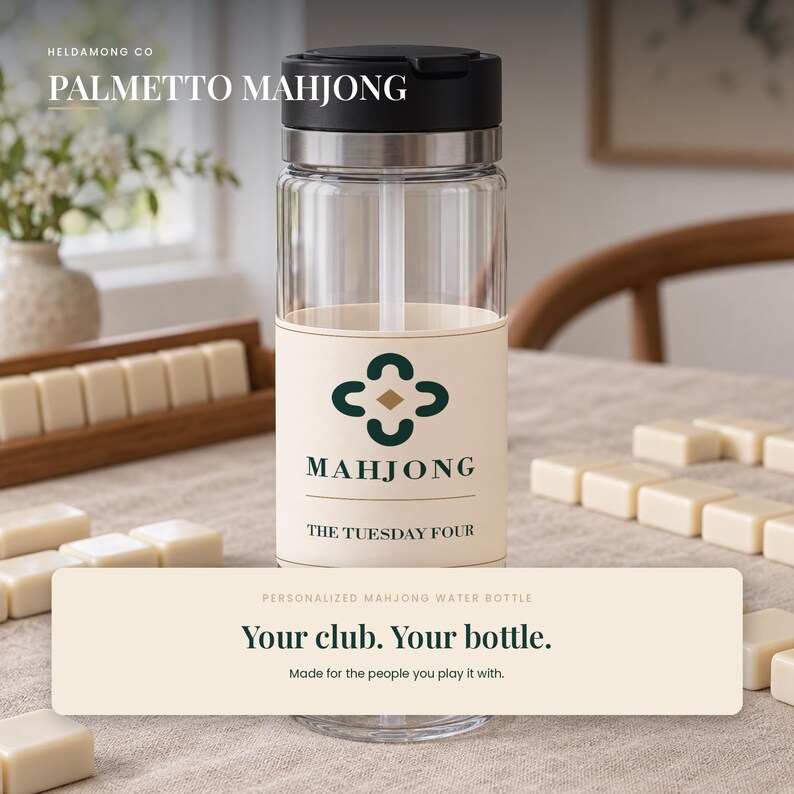 Peut inclure: Une bouteille d'eau transparente avec un couvercle noir et une &eacute;tiquette cr&egrave;me arborant une ic&ocirc;ne de tr&egrave;fle vert fonc&eacute;, le texte "MAHJONG", "THE TUESDAY FOUR" et "Your club. Your bottle. Made for the people you play it with."