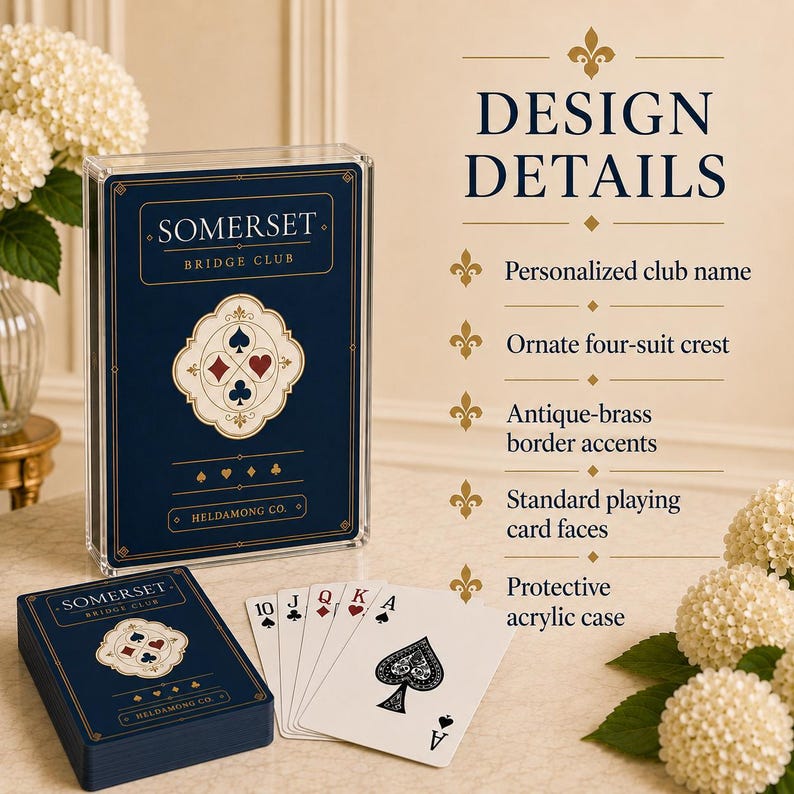 Puede incluir: Una baraja de cartas en un estuche de acr&iacute;lico transparente, con una caja azul oscuro que muestra el texto Somerset Bridge Club y Heldamong Co. Las cartas presentan un escudo ornamentado de cuatro palos, bordes de lat&oacute;n antiguo y caras est&aacute;ndar.