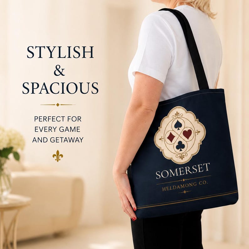 May include: A dark blue tote bag with black shoulder straps featuring a cream-coloured emblem with four playing card suit symbols. The text reads STYLISH & SPACIOUS, PERFECT FOR EVERY GAME AND GETAWAY, SOMERSET, and HELDAMONG CO. with a fleur-de-lis.
