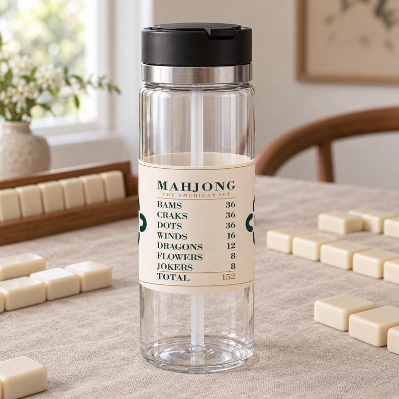 Puede incluir: Una botella de agua de pl&aacute;stico transparente con tapa negra y pajita blanca. Una etiqueta de color crema envuelve el centro, con el texto MAHJONG THE AMERICAN SET, seguido de una lista de categor&iacute;as de juego y valores num&eacute;ricos que suman 152.