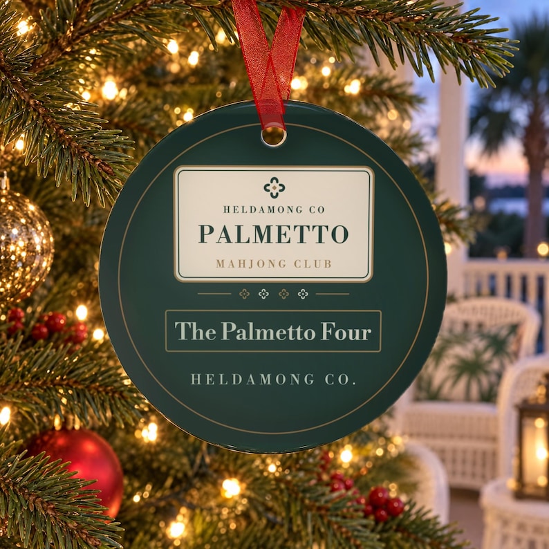 May include: A round dark green ornament with a red ribbon hanger. The center features a cream-colored label with the text HELDAMONG CO PALMETTO MAHJONG CLUB, followed by the text The Palmetto Four and the brand name HELDAMONG CO. at the bottom.