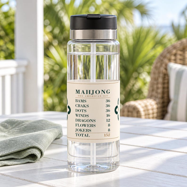 Puede incluir: Una botella de agua de pl&aacute;stico transparente con tapa negra y pajita blanca. Una etiqueta beige en el frente presenta el texto MAHJONG THE AMERICAN SET, seguido de una lista de categor&iacute;as de juego y n&uacute;meros, terminando con un total de 152, flanqueado por iconos de color verde oscuro.