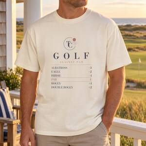 May include: A cream-coloured short-sleeve t-shirt featuring a graphic print with the text GOLF AGAINST PAR and a list of golf scoring terms including Albatross -3, Eagle -2, Birdie -1, Par E, Bogey +1, and Double Bogey +2 with a circular logo.