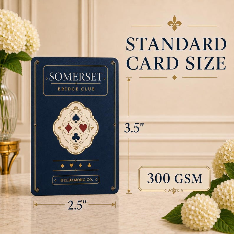 Puede incluir: Una carta de juego azul oscuro con detalles dorados, con el texto SOMERSET BRIDGE CLUB y HELDAMONG CO. La carta muestra un emblema central con cuatro palos. Las dimensiones indicadas son 8,89 cm por 6,35 cm con 300 GSM.