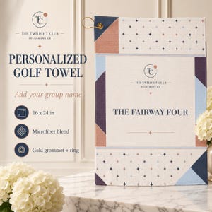 May include: A rectangular microfiber golf towel featuring a geometric pattern in navy blue, light blue, and muted peach. The center displays the text THE TWILIGHT CLUB HELDAMONG CO and THE FAIRWAY FOUR. It includes a gold grommet and metal ring.