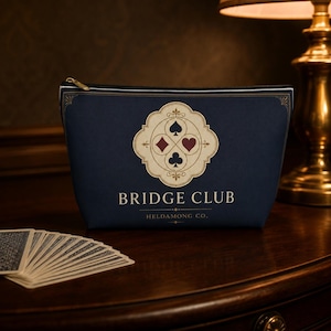 May include: A dark navy blue zippered pouch featuring a cream-colored emblem with four playing card suit symbols: spade, diamond, heart, and club. The text BRIDGE CLUB and HELDAMONG CO. is printed in white below the emblem. A fan of playing cards is visible.