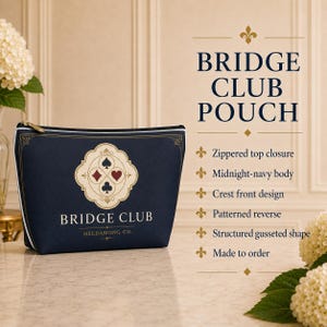 May include: A midnight-navy zippered pouch featuring a cream-colored crest with four card suit symbols and the text BRIDGE CLUB HELDAMONG CO. The structured, gusseted pouch has a white piped edge and a patterned reverse side for a classic look.