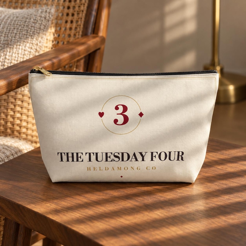 May include: A cream-colored canvas zippered pouch featuring a dark red number 3 inside a thin gold circle, flanked by a small heart and diamond. The text reads THE TUESDAY FOUR HELDAMONG CO in dark brown lettering with a small diamond below.