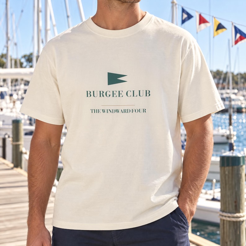 Puede incluir: Una camiseta de manga corta en color blanco roto con un gr&aacute;fico verde oscuro en el pecho. El dise&ntilde;o incluye un icono de bandera triangular sobre el texto "BURGEE CLUB" y "THE WINDWARD FOUR" en una fuente sans-serif de color verde.