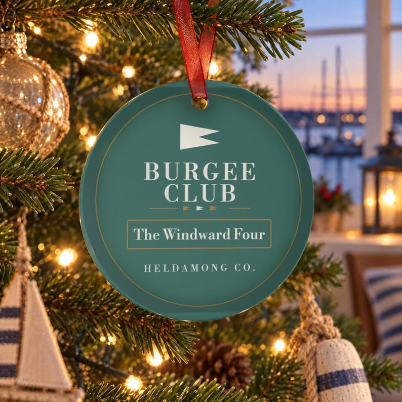 K&ouml;nnte beinhalten: Ein runder, blaugr&uuml;ner Keramik-Weihnachtsbaumschmuck, der an einem roten Band h&auml;ngt. Das Ornament zeigt ein wei&szlig;es Wimpel-Symbol, den Text BURGEE CLUB, den Text The Windward Four in einem rechteckigen Rahmen und den Text HELDAMONG CO. unten.
