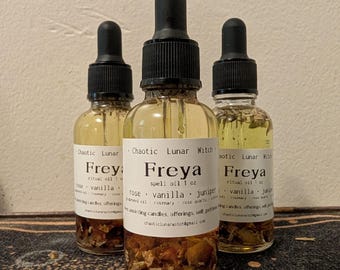 Puede incluir: Tres frascos cuentagotas de vidrio transparente que contienen un líquido dorado con piezas botánicas visibles en la base. Cada etiqueta blanca presenta el texto Chaotic Lunar Witch, Freya spell oil 1 oz, rose, vanilla, juniper y texto adicional.