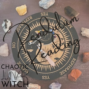 May include: A black and gold pendulum board with the words "Pendulum Reading" written in white cursive. The board has a yin yang symbol in the center and a compass-like design around the edge. The board is surrounded by various crystals and stones.