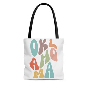 Può includere: Borsa tote bianca con manici neri e un design grafico colorato che dice "OKLAHOMA" in stile retrò.