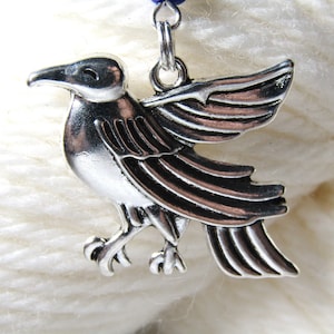 May include: Silver bird charm with detailed wings and a textured finish. The charm is attached to a blue cord.