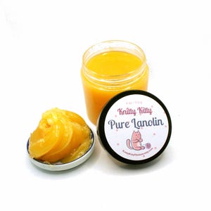 May include: A jar of yellow-orange lanolin, a small dish with lanolin, and a black-lidded jar with the text "Knitty Kitty Pure Lanolin" and a cat graphic. The jar contains 4 oz / 113 g of lanolin.